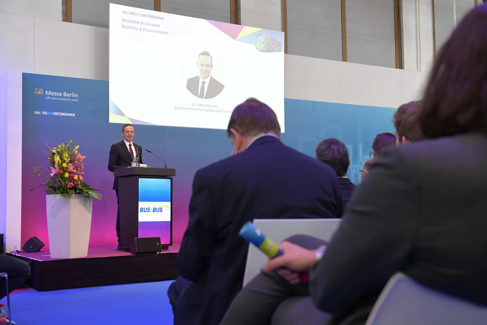 Bundesverkehrsminister Dr. Volker Wissing auf der BUS2BUS 2022. Er steht auf einer Bühne an einem Rednerpult. Im Vordergrund sitzen Zuschauer:innen. 