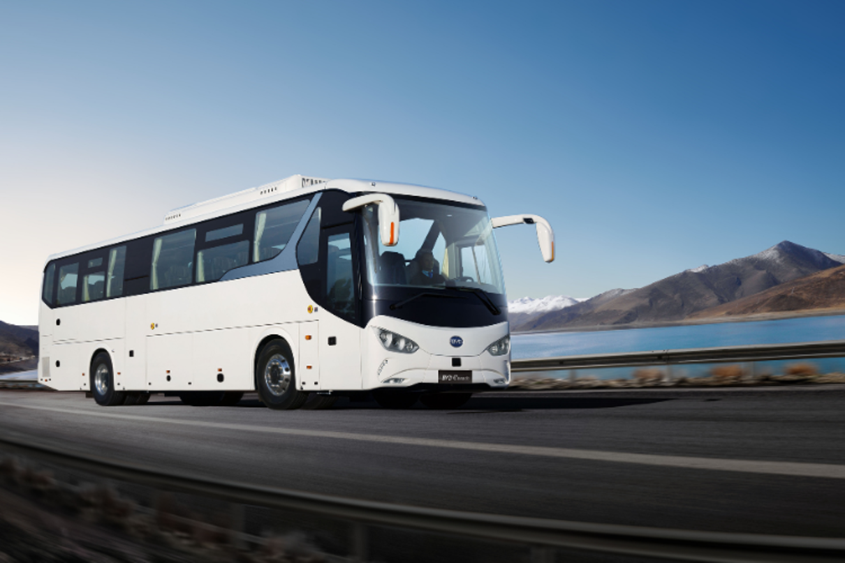 A white e-coach on the highway. In the background are a lake and mountains
