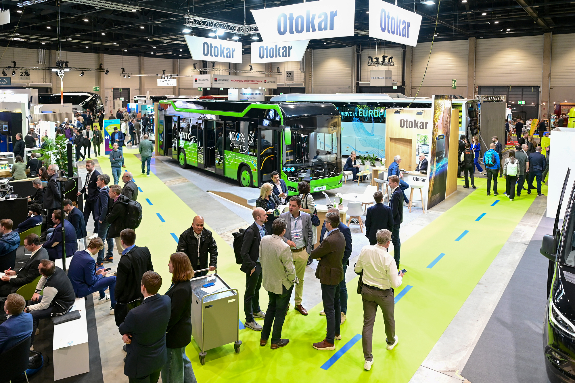 Eine Messehalle mit Bussen unterschiedlicher Hersteller und Fachbesucher:innen der BUS2BUS, die miteinander im Gespräch sind. 